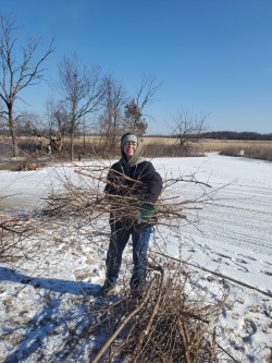A photo of a person holding a bundle of twigs on a snow covered field.