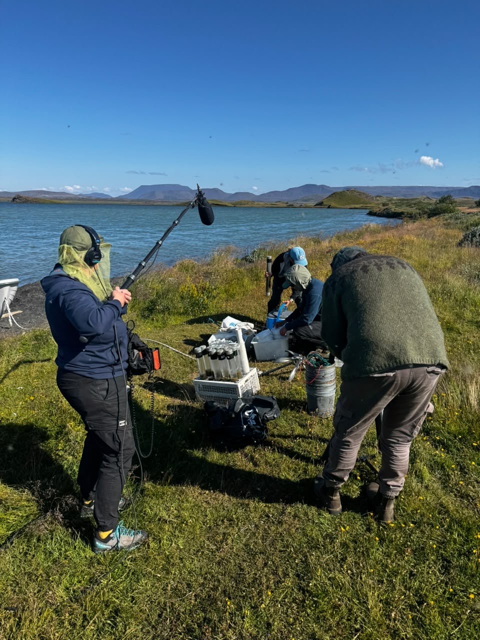 A group of people handling water samples and buckets on a lake shore.